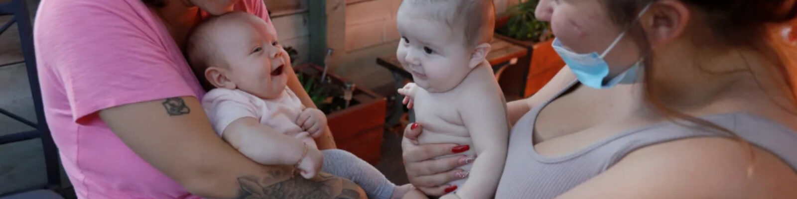 two mothers face each other holding smiling babies