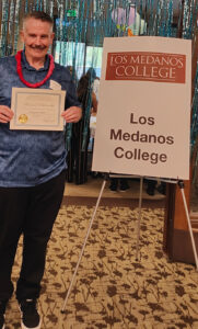 Ben Osborn holding certificate next to sign saying Los Medanos collage
